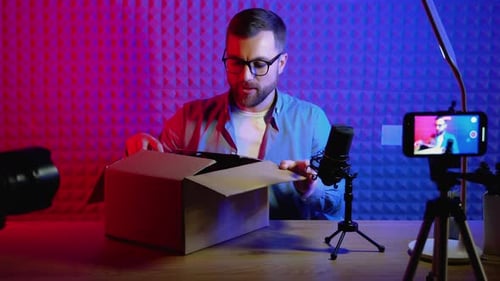 Young Male Technology Blogger Recording Video Blog or Vlog Review of New Smartphone at Home Studio