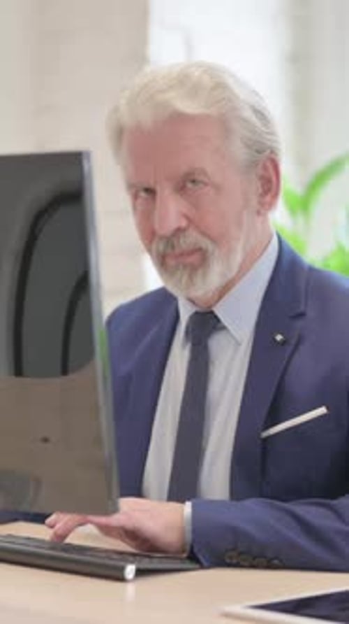 Senior Man Working at Computer Smiles at Camera