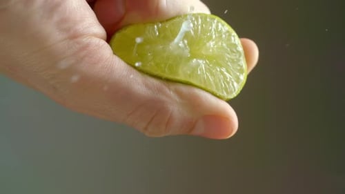 A man squeezes a lime that is cut in half while the juice squirts