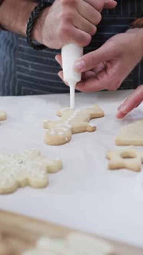 Vertical video of midsection of caucasian man decorating christmas cookies, slow motion