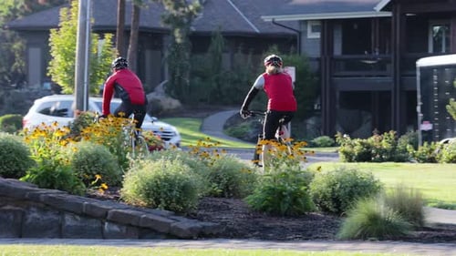 Two cyclists ride through a green community park in Oregon; 4K.