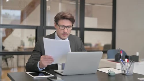 Man Reviews Documents at Desk in Office