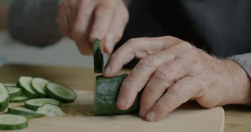 Closeup of Male Hands Chopping Fresh Cucumber on Wooden Board Preparing Salad at Home