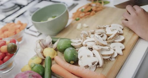 Hands are chopping vegetables on a wooden board in a home kitchen
