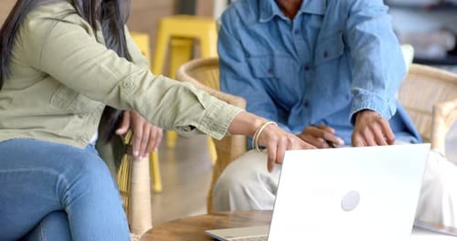 Caméra focalisée sur un ordinateur portable, suscitant divers collègues pointant vers l'écran pour discuter d'un projet dans un café
