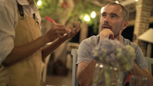 Young couple at cafe enjoying evening meal ordering food from attentive waiter