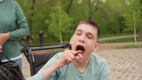 Teen in Wheelchair Eats Pretzel in Park