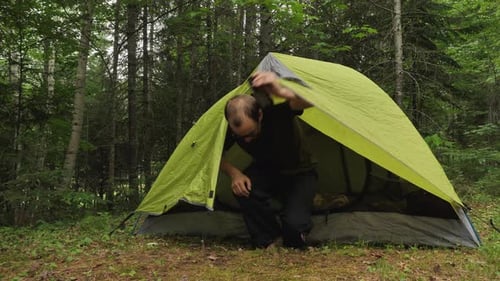 Man getting out of a small camping tent's door.