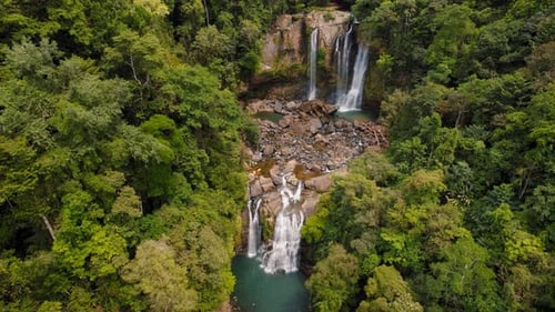 Aerial view of twin tropical waterfalls surrounded by dense green rainforest trees