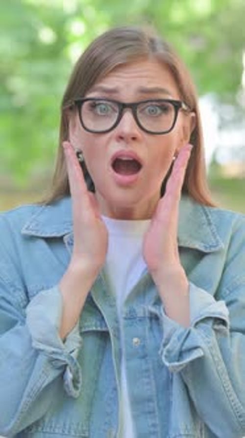 Excited young woman celebrates success outdoors, portrait view