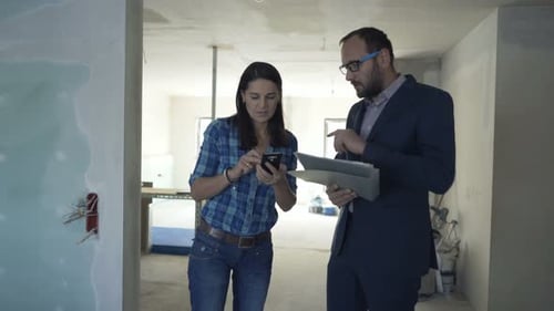 Real estate agent and client reviewing documents at new home with smartphone