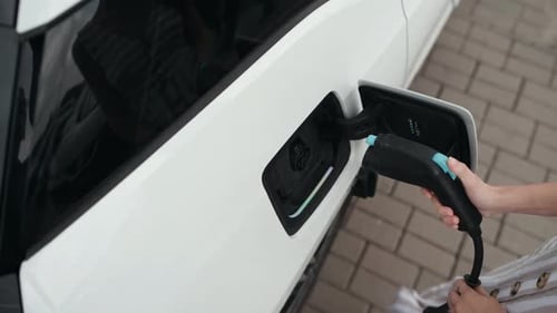 Frau steckt das Ladegerät in die Steckdose ihres modernen neuen Elektroautos