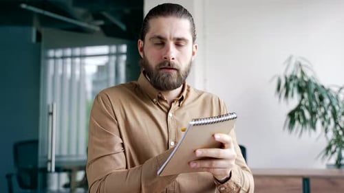 Webcam view. Businessman watching video call conference takes notes in notebook looking at camera