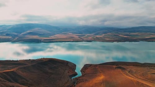 Aerial Views of Lake, Arid Hills and Mountains Under Dramatic Clouds