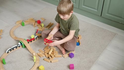 Boy Plays with a Wooden Train Set Indoors