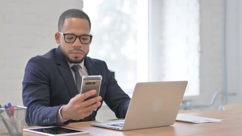Young Adult Man Works on Laptop and Phone
