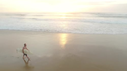 4k Drone Footage Of Attractive Surfer Man Walking On Beach With Surfboard At Sunrise With Ocean W...