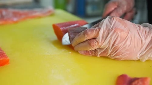 Sea salmon is cut by the hands of a chef in white gloves on thin slices to prepare a dish