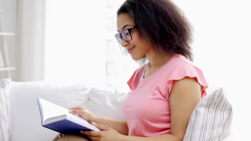 Leisure, Literature And People Concept - Smiling African American Young Woman In Eyeglasses Readi...
