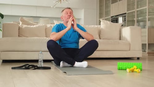 Mature Man Meditates on Yoga Mat at Home