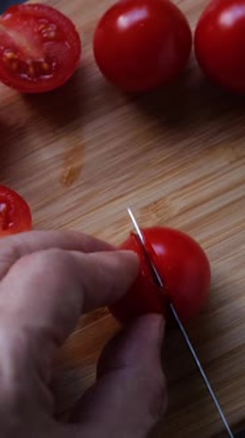 Top view of man hands cutting cherry tomatoes on the cutting board.