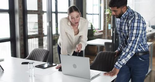 Young Caucasian woman and Asian man review business content on a laptop in an office