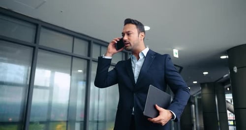 Stressed businessman arguing on phone walking in modern office