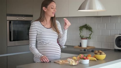 Pregnant Woman Prepares and Eats Fruit in Kitchen
