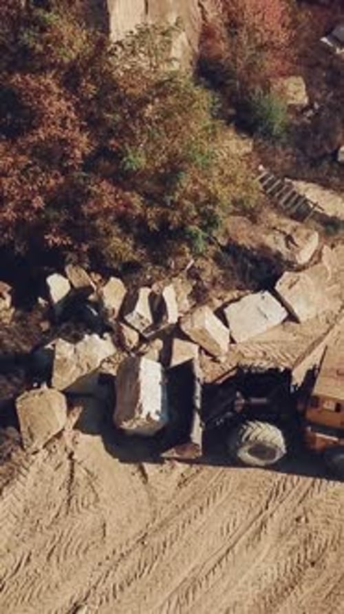 Ein gelber Bulldozer mit einem Eimer trägt einen großen Stein in der Nähe eines Sandsteinbruchs.