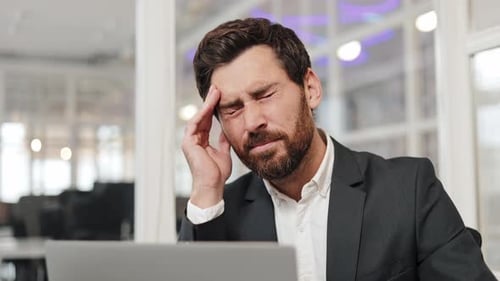Stressed Businessman Has a Headache While Working on Laptop in Office