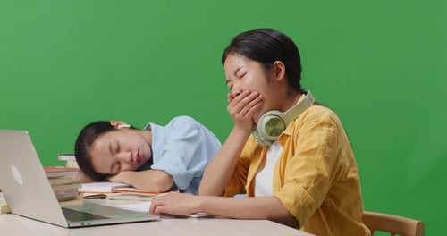 Asian Woman Student Writing And Yawning While Her Friend Is Sleeping With Laptop In The Green Screen