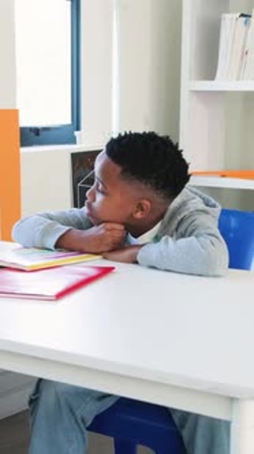 Vertical video: Flipping notebook hooded boy closing it resting chin gazing window at desk thinking