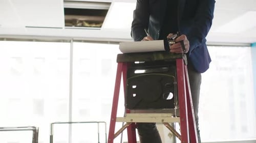 Architect Making Notes on Ladder in Empty Office Space Adult