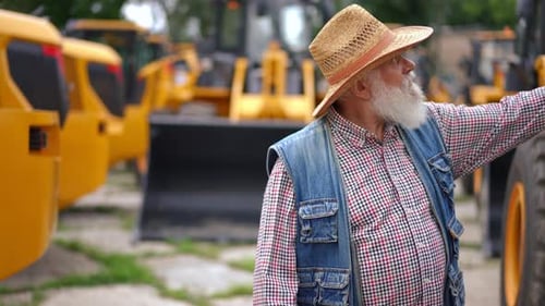 Bearded Concentrated Senior Man Walking on Outdoor Market of Agricultural Vehicles Choosing New