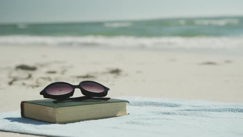 Close up of book, sunglasses and towel on beach, in slow motion, with copy space