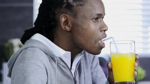 Man drinking orange juice through straw indoors