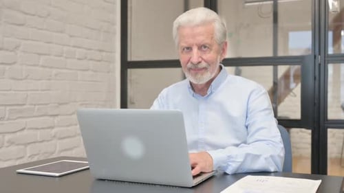 Senior Businessman Smiling at Camera while Working on Laptop in Office