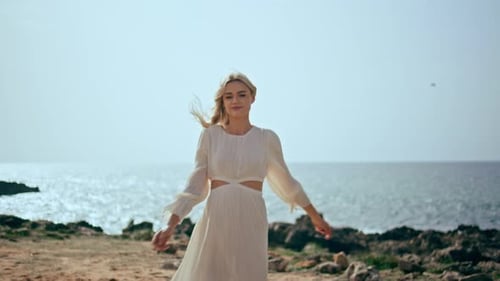 Gentle woman in white dress walking on ocean shore at beautiful sunset light