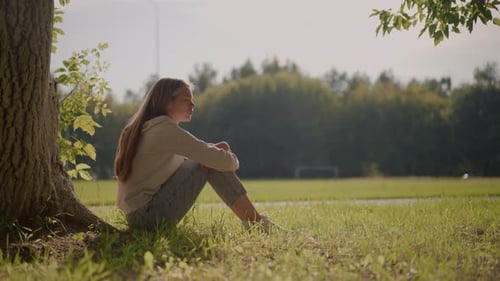 Thoughtful Woman Sitting on Grassy Field with Sunlight and Peaceful Background