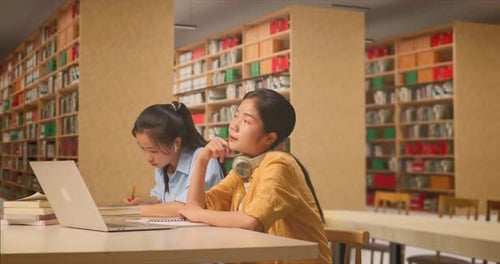 Student Thinking Then Raising Her Index Finger While Sitting With Classmate In The Library