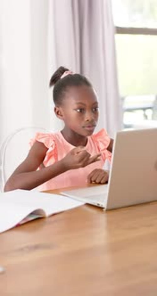 Vertical video: African child in pink top watching laptop lesson, counting on fingers with notebook