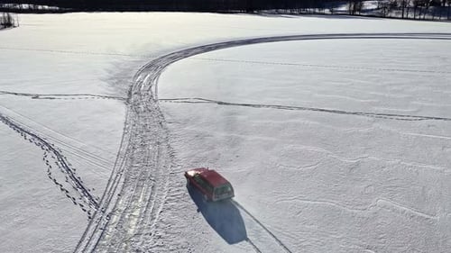 Aerial View of Car Drifting Across Snowy Field with Tire Tracks
