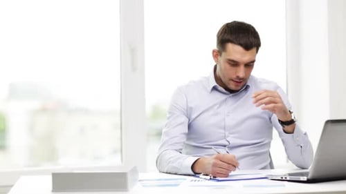 Busy hispanic businessman working on laptop with financial reports in modern office