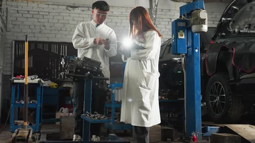 Professional Measuring Engine Thickness While Colleague Records Data in Automotive Shop