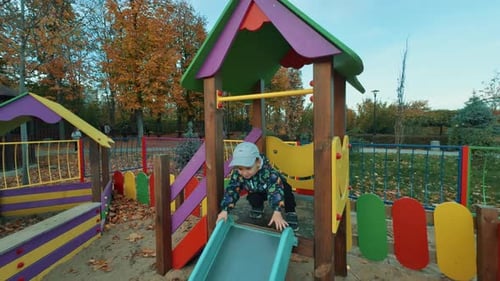 Happy smiling kid sits on the slide tapping his feet. Energetic cheerful child on the playground.