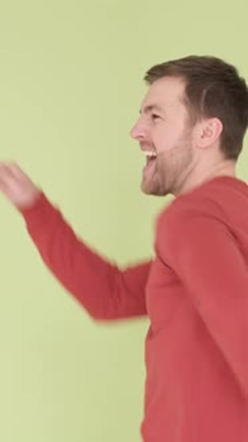 A Young Guy in an Orange Sweater is Dancing Funny Isolated on the Background in the Studio