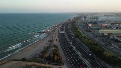 Aerial view of a coastal road with multiple lanes next to a beach, with buildings on the other side,