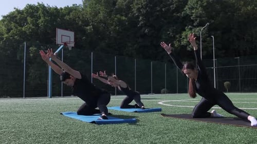 Three Women Practicing Group Pilates on a Green Sports Field