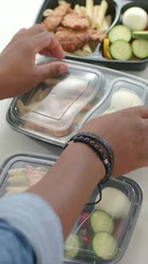 Homme atteignant et scellant les couvercles transparents de trois contenants de préparation de repas contenant des penne et du poulet