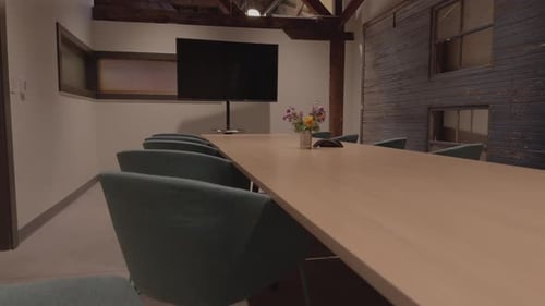 Slow rising reveal from behind chair toward modern conference table and meeting display